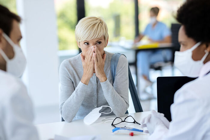 A worried woman speaking with doctors in masks, reflecting a patient's experience with medical procedures.
