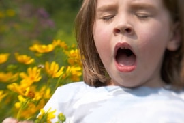 A girl sneezing while holding flowers in her hand.