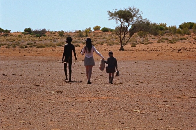 Three people shown from the back walking through a vast dessert
