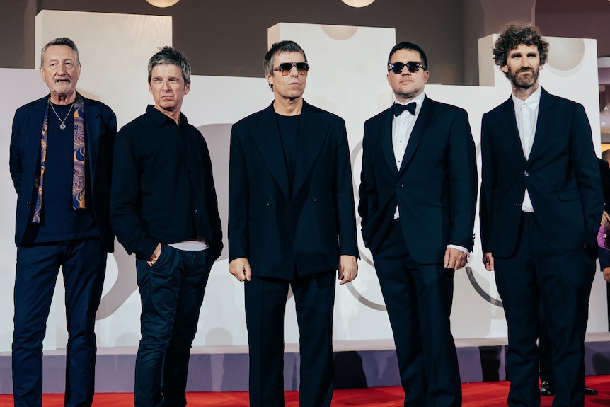five older men in suits and fashion wear pose on the red carpet of Venice International Film Festival