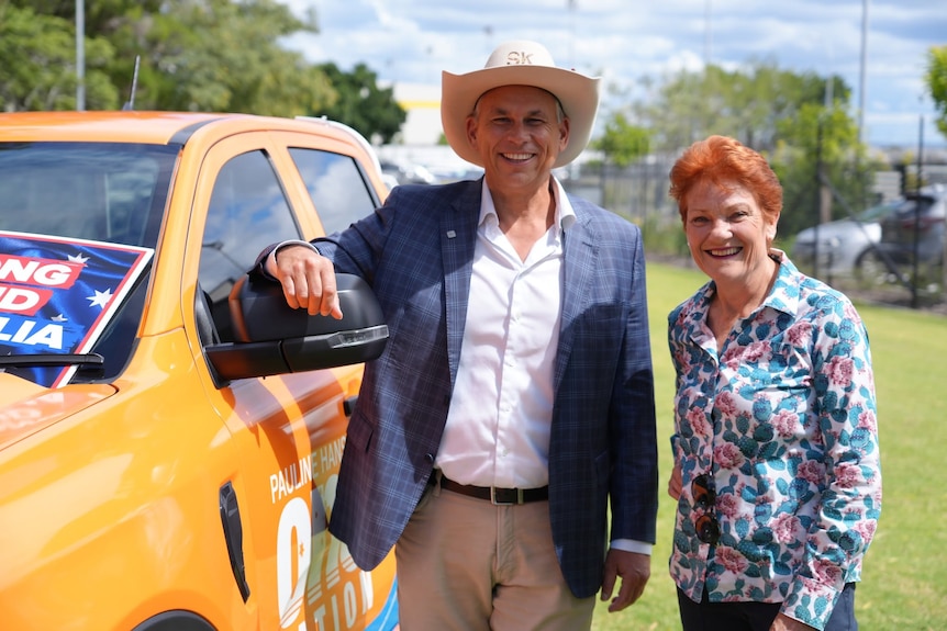 a man wearing an akubra smiling with a redheaded woman next to an orange Ute