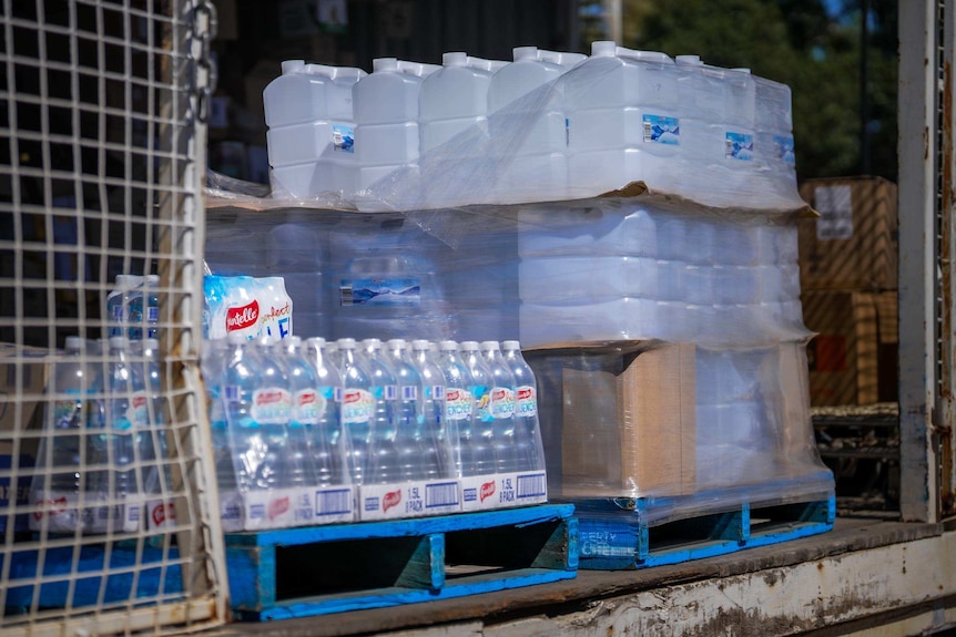 Pallets stacked with 10 litre and 1.5L bottles of water sit on the loading deck of a shop after delivery.