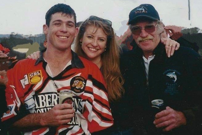 A woman smiles between two men drinking a beer at a sporting event.