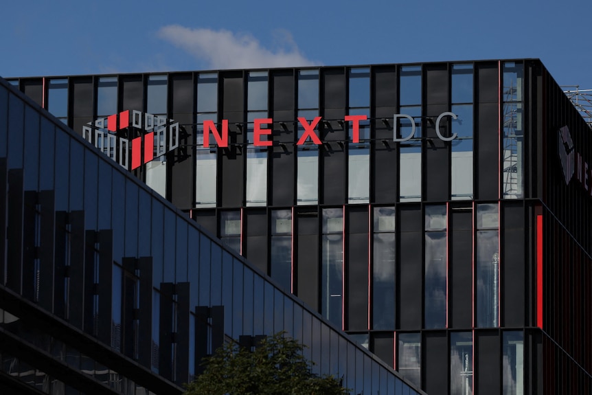 A building with a facade of black cladding and dark glass windows, and a sign saying "NextDC".