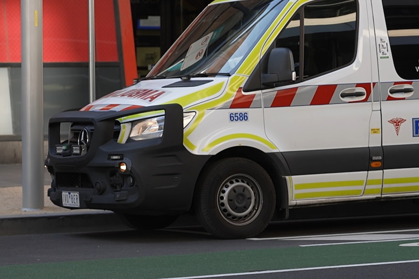 A white ambulance vehicle with red and grey stripes and the word "paramedic" in blue is parked on a city street.