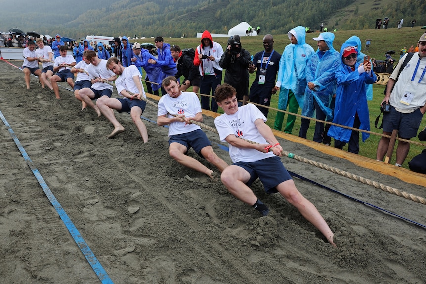 men heave into mud, pulling a rope.