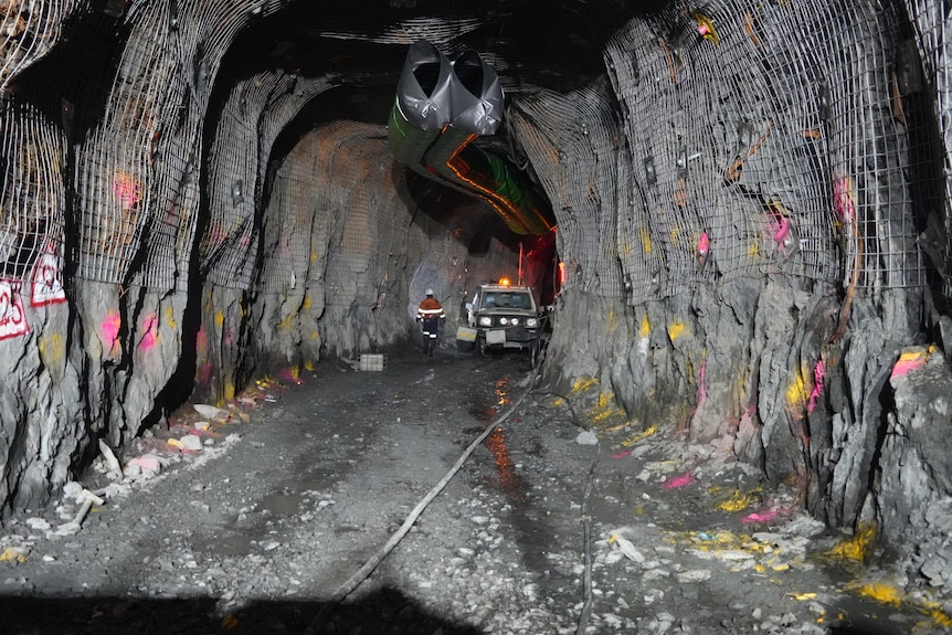 A miner stands at the end of a long mining tunnel 