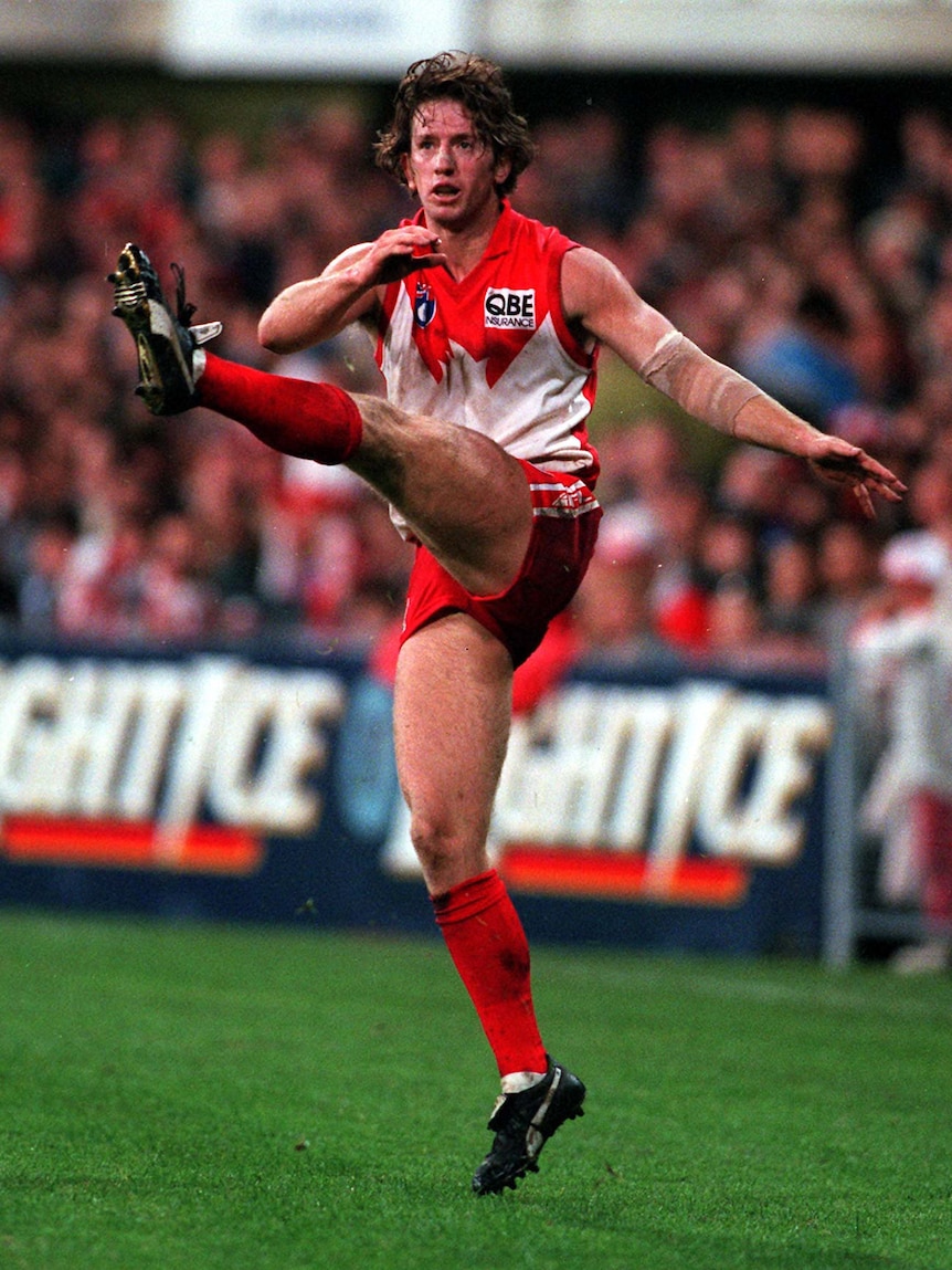 A Sydney Swans player looks downfield with leg extended after taking a big kick from the wing.