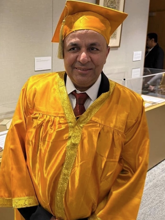Mr Bhushan smiling in a bright yellow graduation outfit.