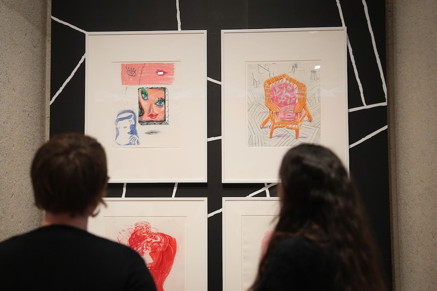 Two people looking at four color lithographs in a neo-cubist style hanging on the wall of an art gallery.