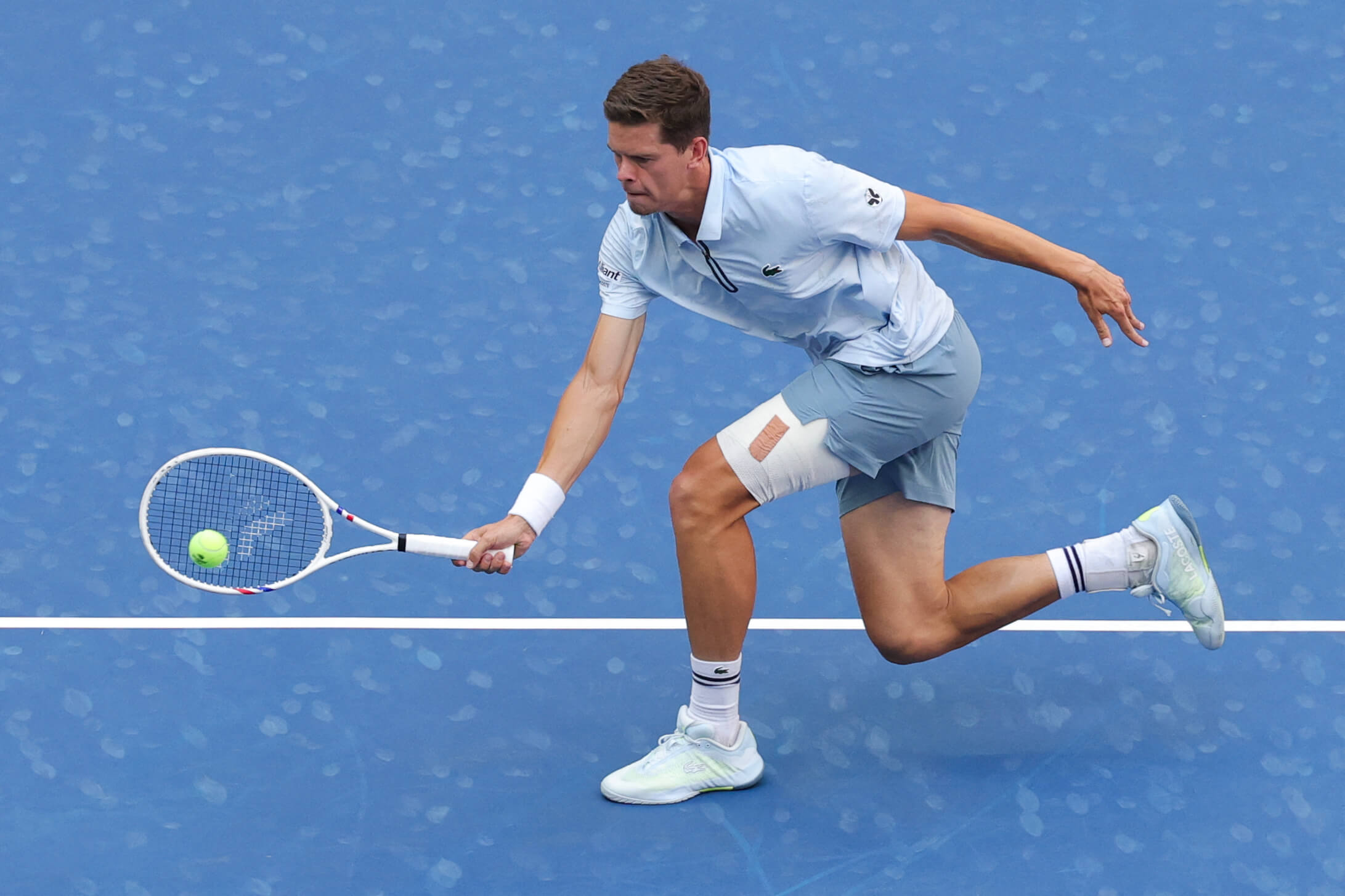 Alexander Blockx stretches low to get a ball on a tennis court.
