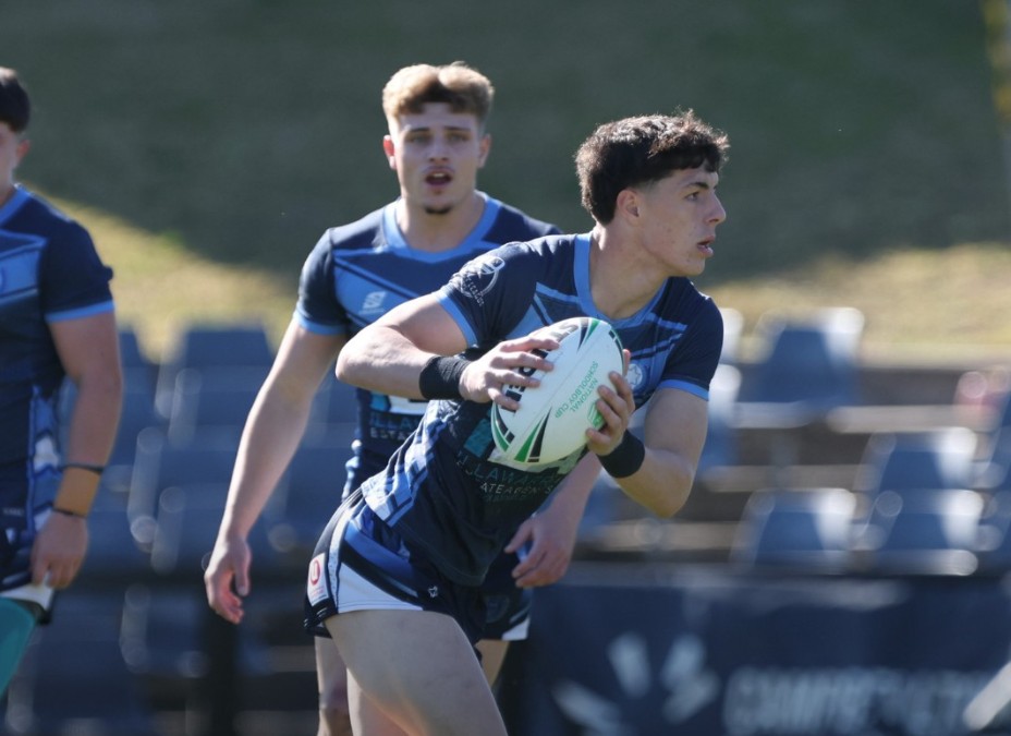 A young schoolboy rugby league player in uniform playing rugby league with the ball in his hand and looking to pass to a team mate