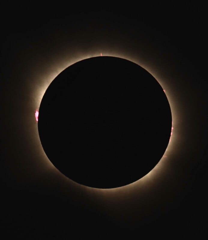 A total solar eclipse shows the moon silhouetted against the sun, with a glowing corona and bright red solar prominences.