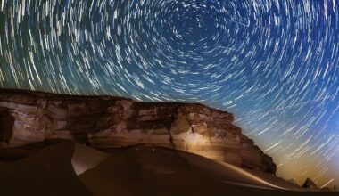 Star trails circle above a desert at night as meteors streak through the sky.