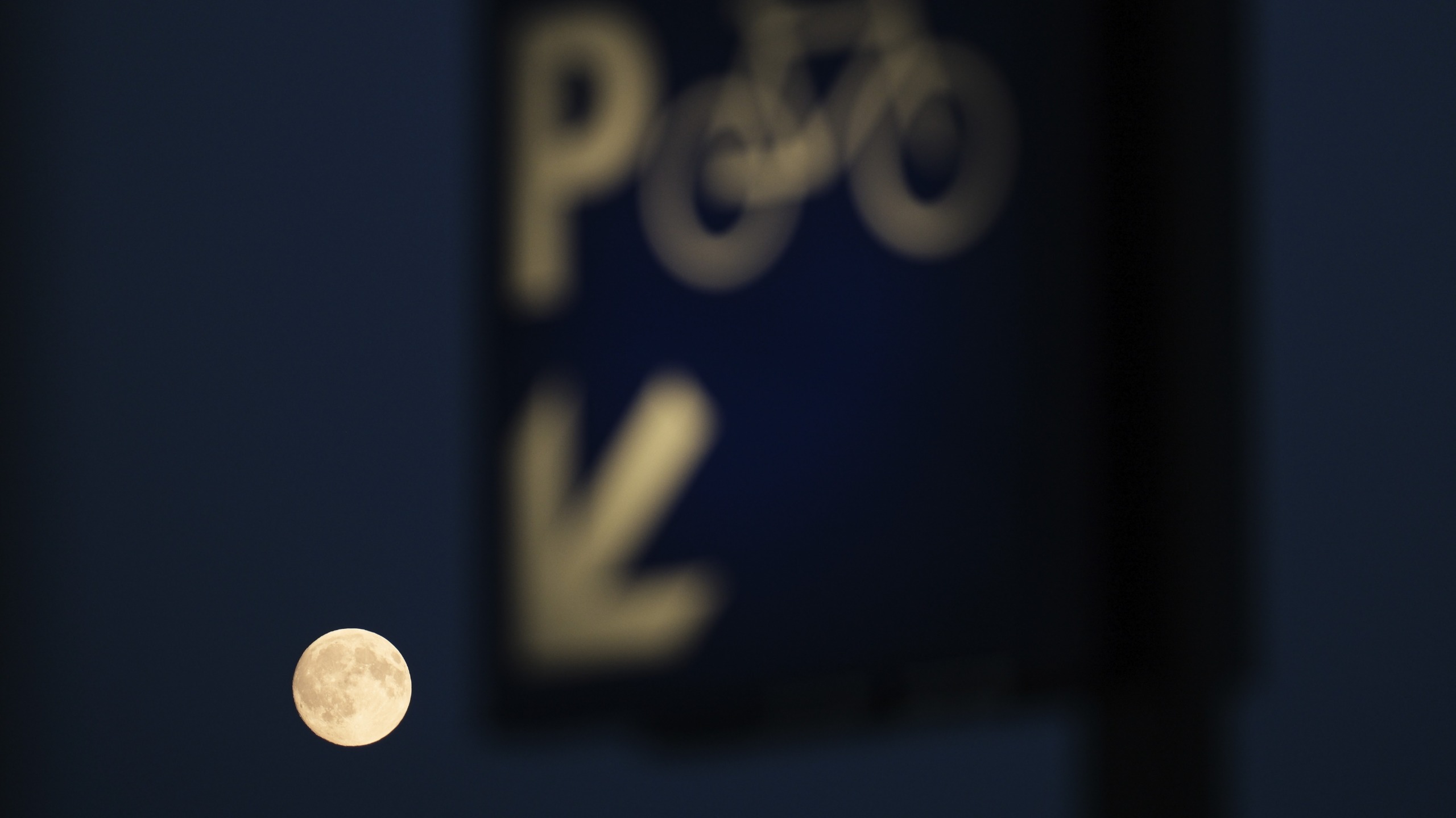 A large silvery moon appears below a blue bicycle parking sign as it rises behind the Inkpot building in Utrecht, Netherlands.