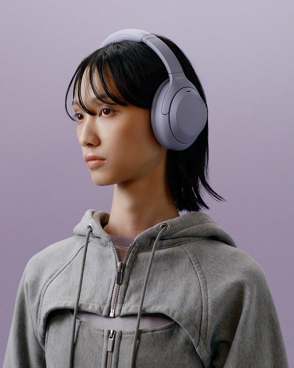 A person in a gray sweatshirt wearing lavender Sony WH-1000XM4C headphones.