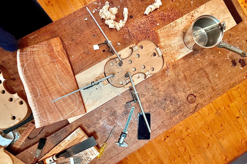 Aerial image of a wooden violin, laying on a workbench, in bits.