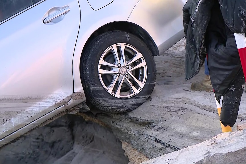 A silver car with the front half in a deep sinkhole.