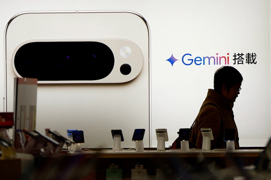 A silhouette of a man is seen in front of a full-wall smartphone ad with the Gemini logo next to it