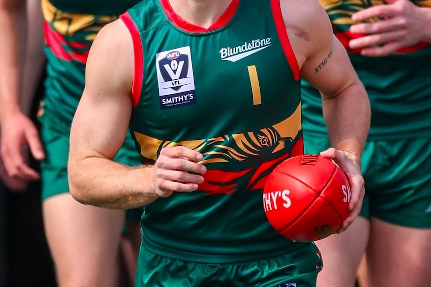 Three unidentified Tasmania Devils AFL players running towards camera.