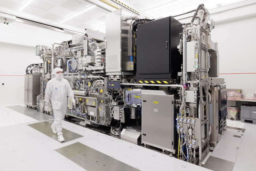 A technician in a cleanroom stands beside a large ASML EUV lithography machine used to manufacture advanced semiconductor chips.