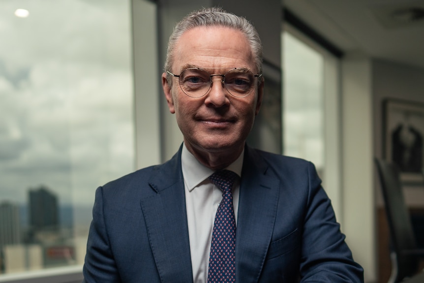 Christopher Pyne, with grey, slicked-back hair, wears a navy suit. He is near a window.