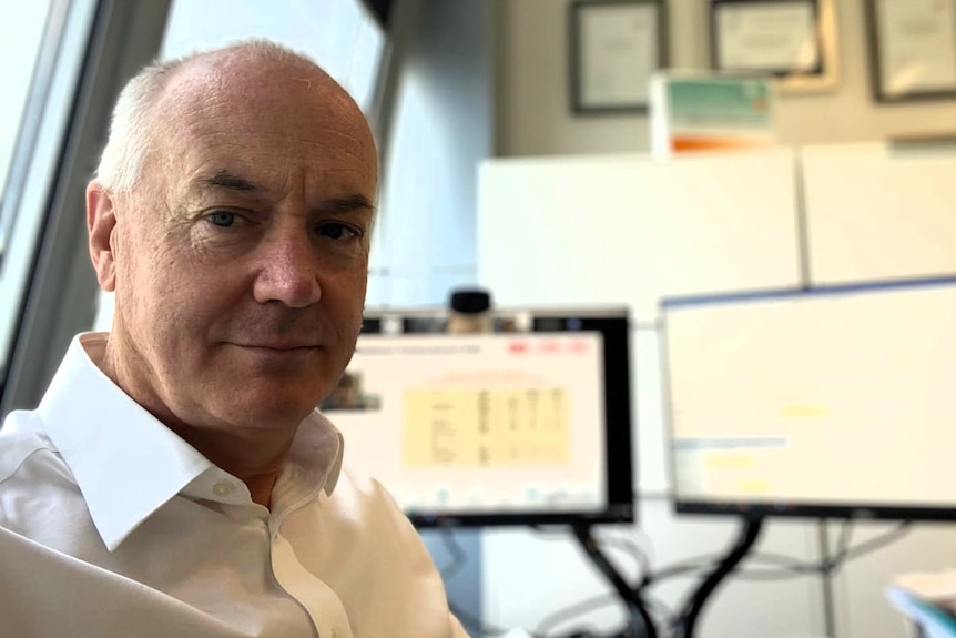 A bald white man with a white collared shirt sitting at a computer