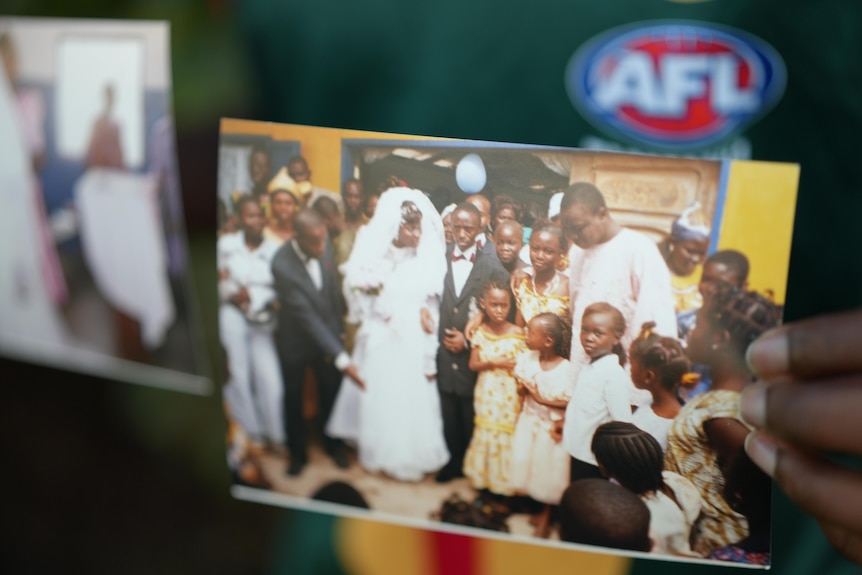 A photo of a hand holding two photos, one is blurry, one is of children crowding around a bride and groom.