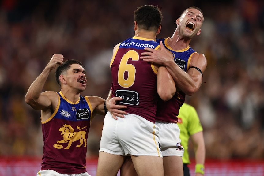 Three players in red and blue celebrate an AFL win