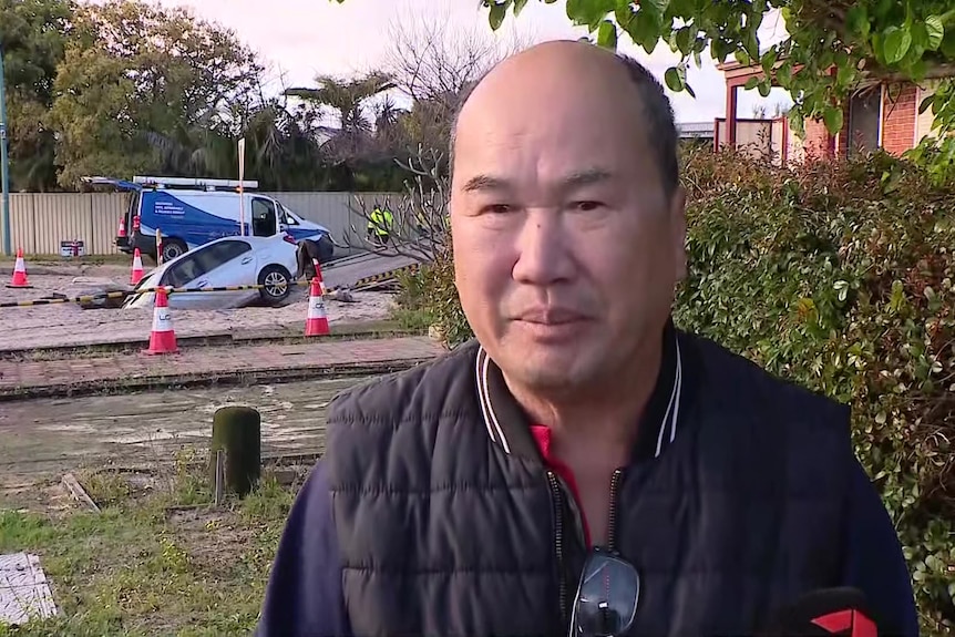 Fred stands in front of a car which has fallen into a sinkhole