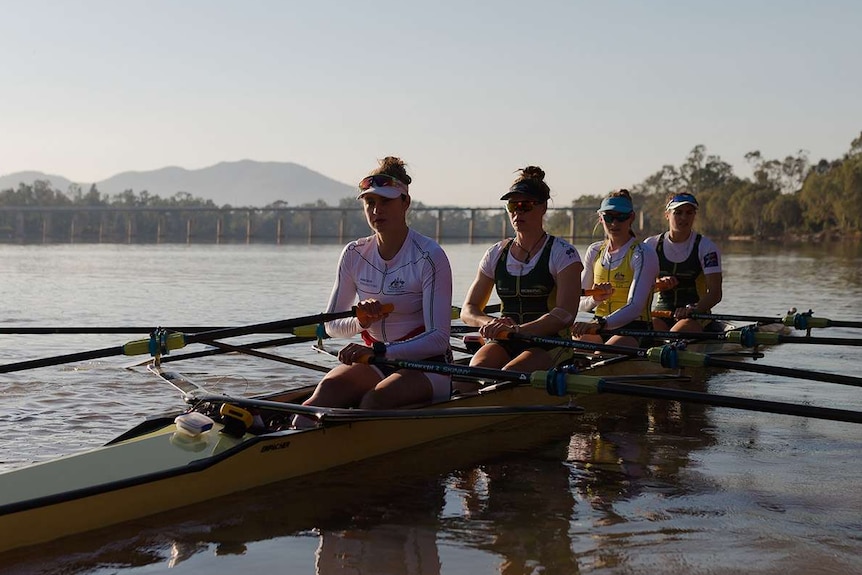 Four women in a rowing boat with barrage in the background