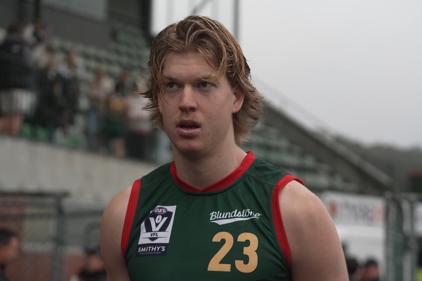 A blonde man wears a green and red football jumper.