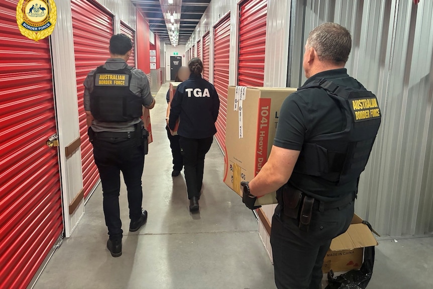 Uniformed police officers carry cardboard boxes through a storage facility.