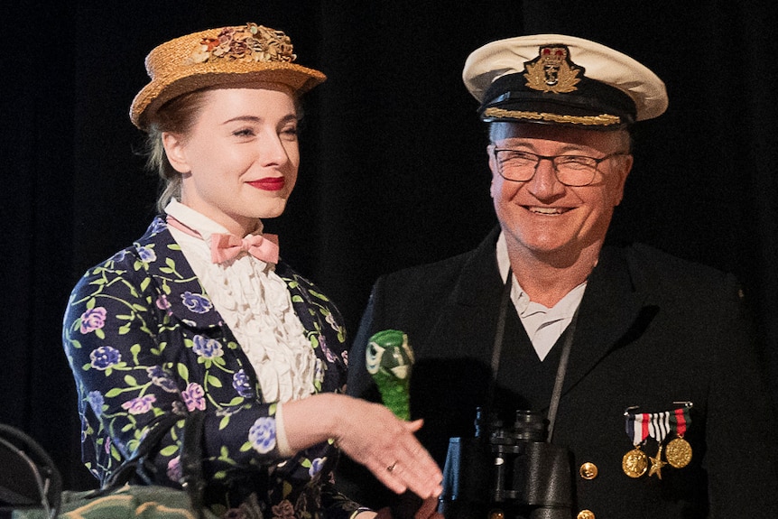A young woman dressed as Mary Poppins stands with an older man wearing a naval uniform.