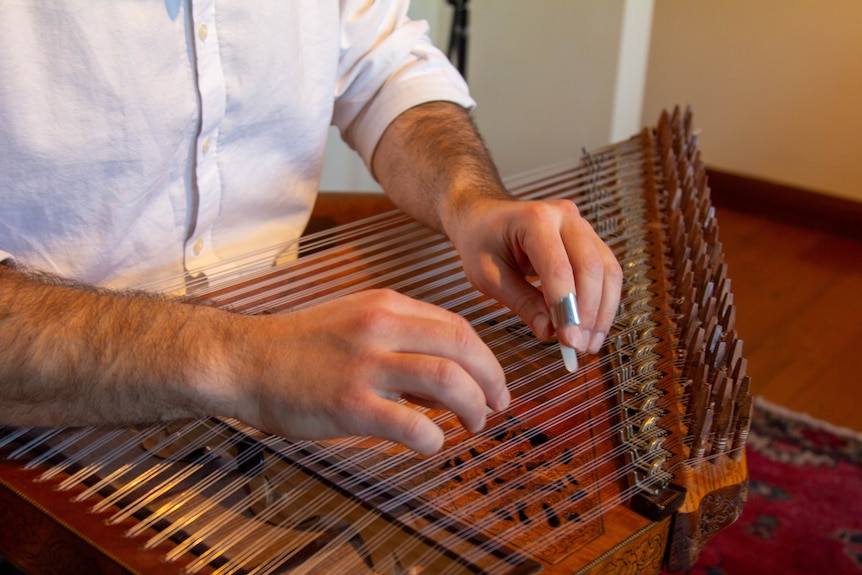 A close-up of a stringed instrument being plucked by two male hands.