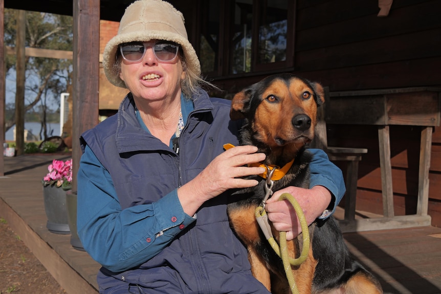 Woman sitting embraces a young working dog while holding a leash.
