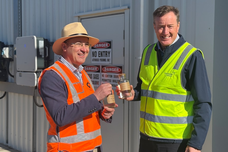 Two men in construction safety vests hold jars of water with labels showing its treated wastewater  