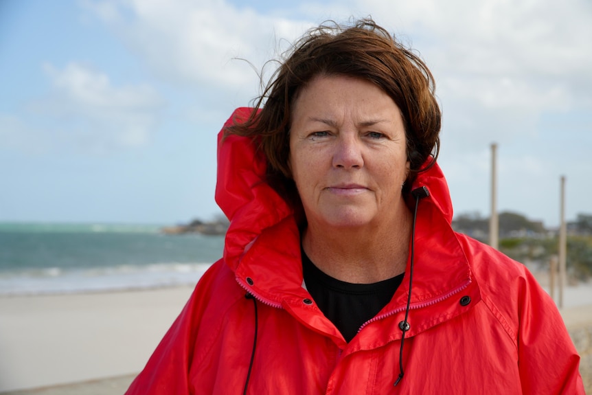 A lady with brown hair wears a bright red jacket at the beach