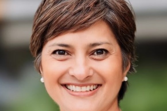 A woman with pearl earrings wearing a white top.