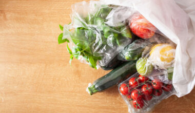 Various fresh vegetables and fruits in plastic bags on a wooden surface.