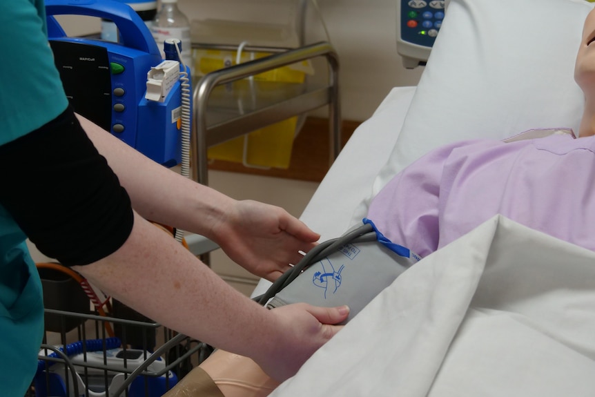 A nursing student practices doing a medical test on a dummy patient.