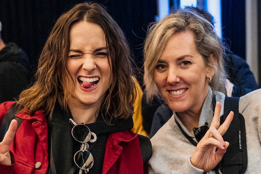 Two white women holding up peace signs, one sticking her tongue out