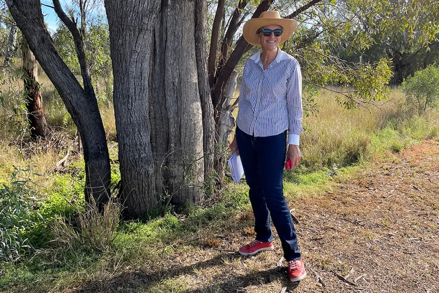 A woman stands next to a tree smiling.