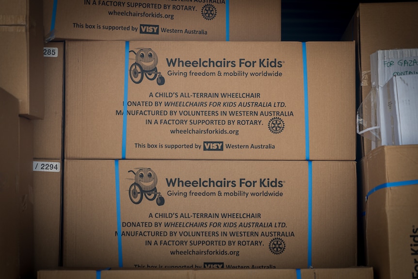 Large cardboard boxes are piled high. The wording reads: Wheelchairs For Kids.