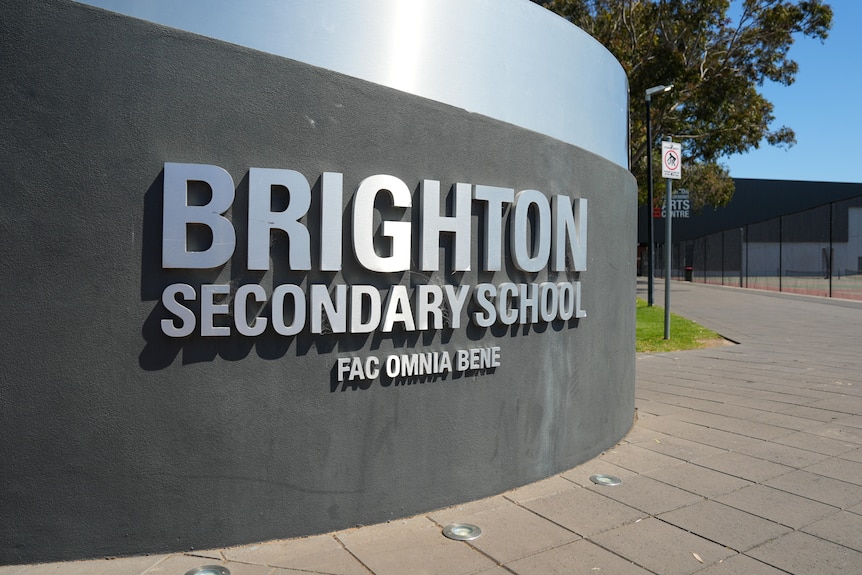 A Brighton Secondary School sign, in reflective silver text on a concrete wall.