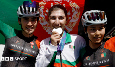 Fariba Hashimi pretends to bite her medal after winning the Aichi-Nagoya Asian Games women's cycling road race silver in Shinshiro, as she stands between two Afghanistan fellow riders