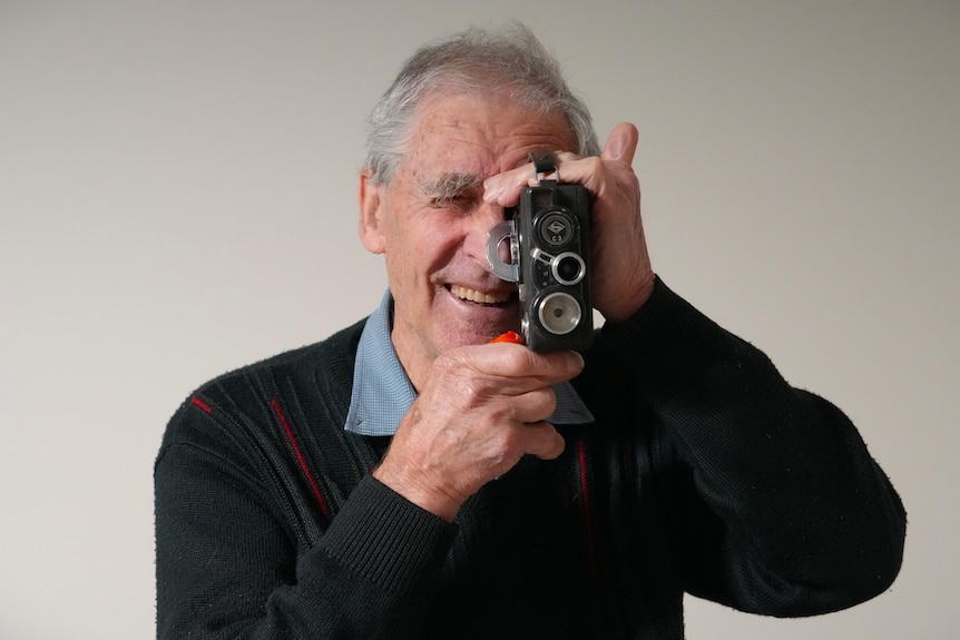 man holds old camera and smiles