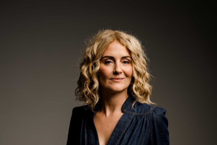 A blonde woman in blue dress looking at the camera.