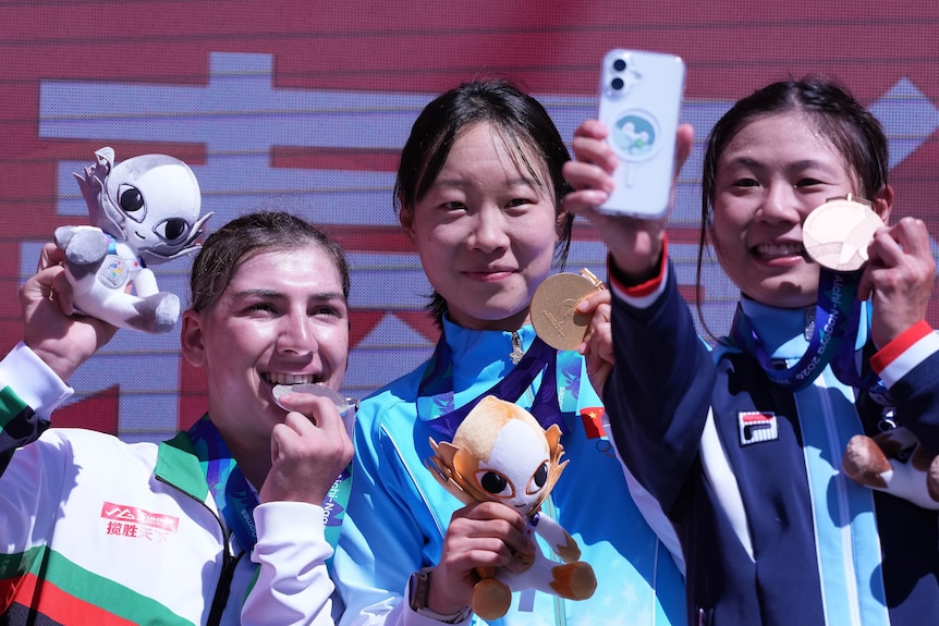 Three cyclists pose with their medals on a podium.