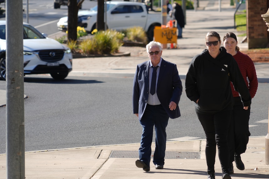 Man in a suit with two women walking on the footpath.